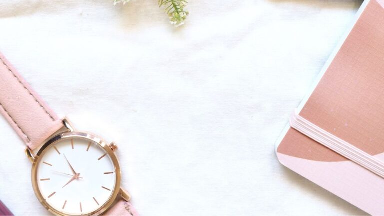 Flachlay mit Armbanduhr, rosa Notizbuch und Dekoration auf hellem Untergrund – Stimmung von Struktur, Zeitmanagement und Selbstorganisation.